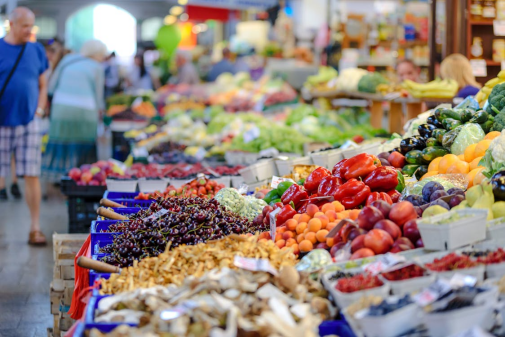 Colorful fresh vegetables on a market stall ready for local restaurant sourcing, including leafy greens, peppers, and root vegetables.